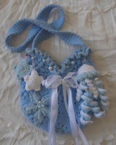 a blue crocheted purse with white bows and beads on it's side