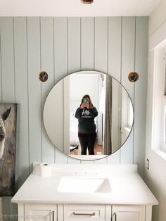 a woman taking a selfie in front of a round mirror on the wall above a bathroom sink