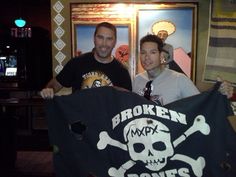 two men standing next to each other holding up a black and white flag with skull and crossbones on it