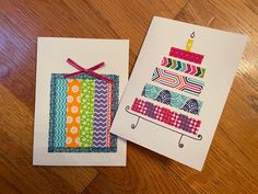 two cards with designs on them sitting on a wooden table next to each other, one has a birthday cake and the other has a candle