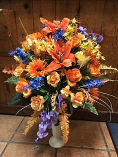 a vase filled with lots of colorful flowers on top of a tile floor next to a wooden wall