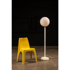 a yellow chair sitting next to a white lamp on top of a cement floor in front of a black wall