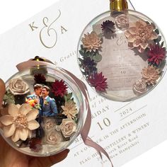 a hand holding an ornament with flowers on it and a wedding card in the background