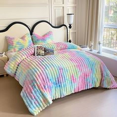 a bed with colorful comforter and pillows in a room next to a window,