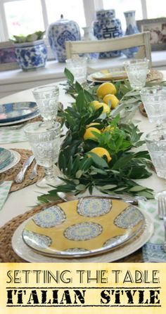 the table is set with plates, silverware and lemons in blue and white dishes