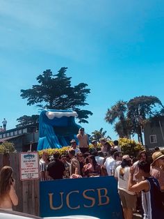 a group of people standing in front of a large blue float on top of a wooden fence