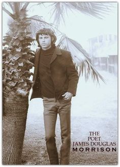 a man standing next to a palm tree with his hands in his pockets and looking at the camera