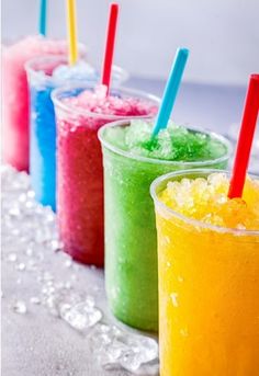 four different colored drinks are lined up on the table with straws in each cup