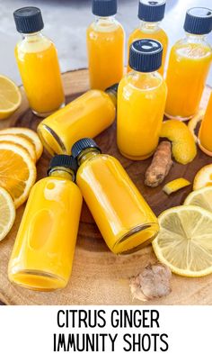 orange juice in glass bottles surrounded by sliced lemons and ginger on a wooden board