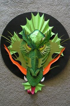 a paper sculpture of a green dragon head on a black circular plate with orange accents