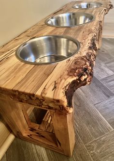 three stainless steel bowls sit on a wooden bench that is made from tree branches and has been turned into a dog bowl stand