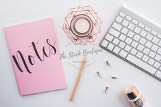 a pink notebook next to a keyboard, candle and other items on a white table