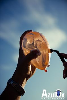 a person holding an orange object in their hand with sky background and clouds behind it