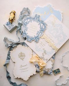 an assortment of wedding stationery items on top of a white table with blue and gold accents