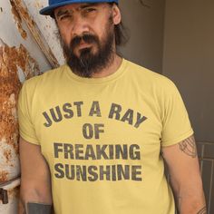 a bearded man wearing a yellow shirt and blue hat standing in front of a rusted wall