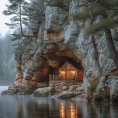 a small cabin built into the side of a rocky cliff by a lake at night