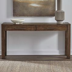 a wooden table with two drawers and a vase on it next to a large painting