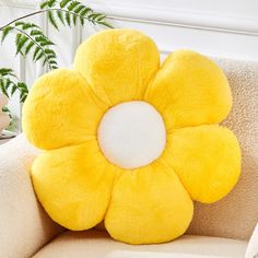 a yellow flower shaped pillow sitting on top of a couch next to a potted plant