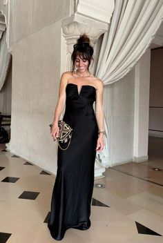 a woman in a black dress standing on a checkered floor with her handbag