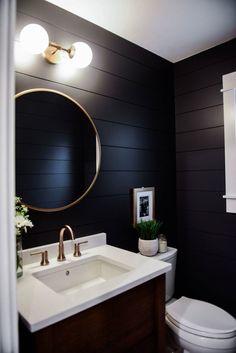 a white toilet sitting next to a bathroom sink under a round mirror on a wall