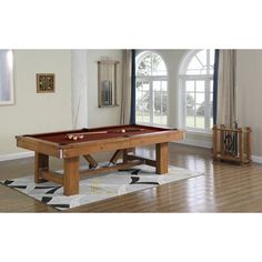 a pool table in the middle of a living room with two windows and a rug on the floor