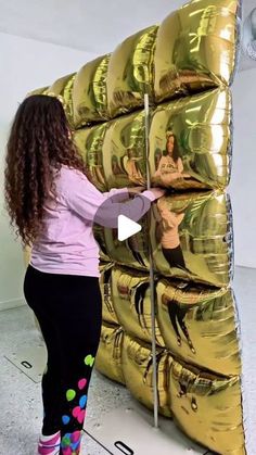 a woman standing in front of a giant pile of gold balloons with pictures on them