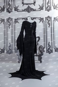 a black dress on display in front of a wall with an ornate frame behind it