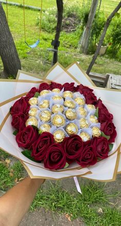 a person holding a heart shaped cake with chocolates on it and roses in the middle