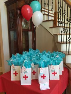 a table topped with blue and white bags filled with red cross gift bags next to a stair case