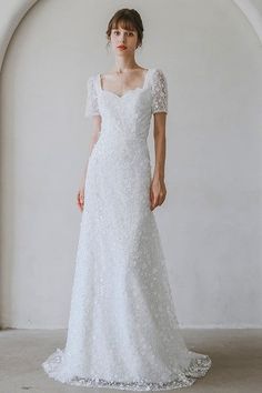 a woman in a white wedding dress standing against a wall with an archway behind her