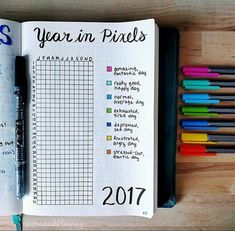 an open notebook sitting on top of a wooden table next to markers and pencils