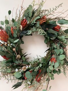 a wreath with green leaves and red flowers on the front is hung on a wall