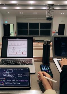 two laptops and a tablet on a table in a room with other electronic devices