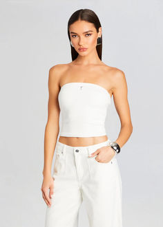 a woman wearing white jeans and a strapless crop top is posing for the camera