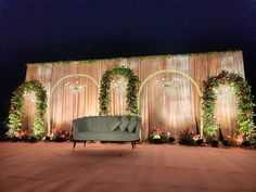 a couch sitting in front of a stage decorated with flowers and greenery at night