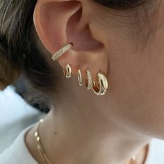 a close up of a person's ear wearing gold earrings and a white t - shirt