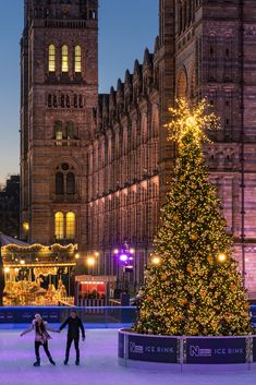 two people skating on an ice rink with a christmas tree in front of a large building