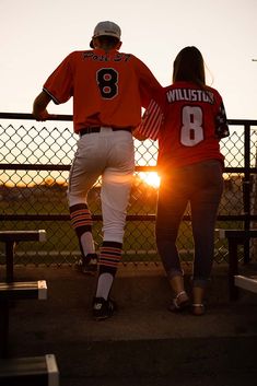 two baseball players standing next to each other on a field at sunset with the sun behind them