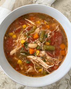 a white bowl filled with soup and vegetables on top of a tablecloth next to a napkin