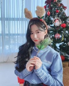 a girl with long black hair wearing a blue sweater and bunny ears holding a green plant