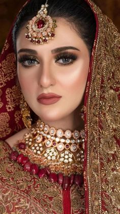 a woman wearing a red and gold bridal outfit with jewelry on her head,