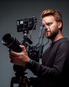 a man holding a camera and looking at the lens on a tripod in front of him