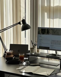 an office desk with a computer, laptop and coffee cup on it in front of a window