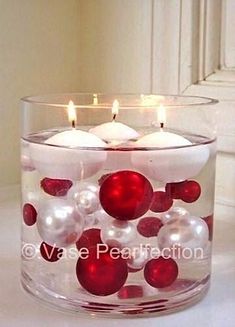 a glass candle holder filled with red and white christmas balls, floating candles and ornaments