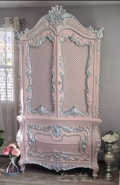 an antique pink armoire with ornate carvings on the front and sides, in a bedroom