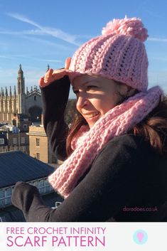 a woman wearing a pink knitted hat and scarf on top of a building with the skyline in the background