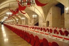 long tables with red and white tablecloths are lined up in an old building