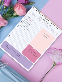 a pink and purple planner sitting on top of a blue table next to some flowers