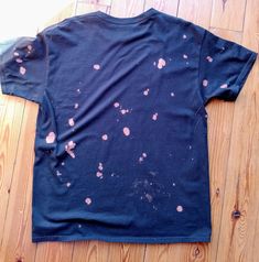 a blue t - shirt with pink spots on it sitting on a wooden floor next to a pair of scissors