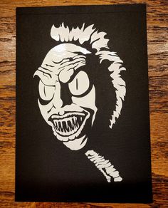 a black and white drawing of a creepy clown on a wooden table with wood grains